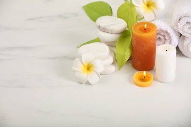 Photo of Spa composition. Burning candles, plumeria flowers, stones and green leaves on white marble table, space for text