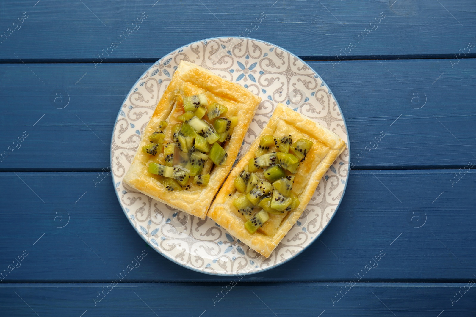 Photo of Fresh tasty puff pastry with kiwi on blue wooden table, top view