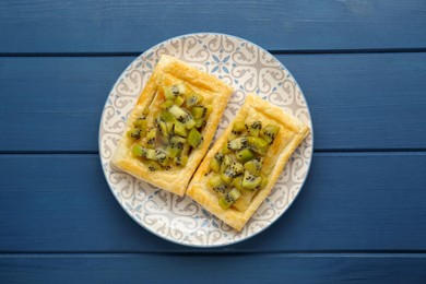 Fresh tasty puff pastry with kiwi on blue wooden table, top view