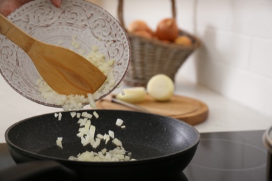 Photo of Woman pouring chopped onion into frying pan in kitchen, closeup