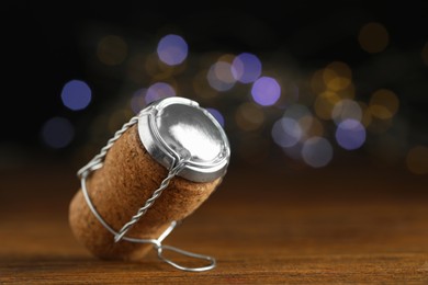 Photo of Sparkling wine cork with muselet cap against blurred festive lights, closeup. Space for text