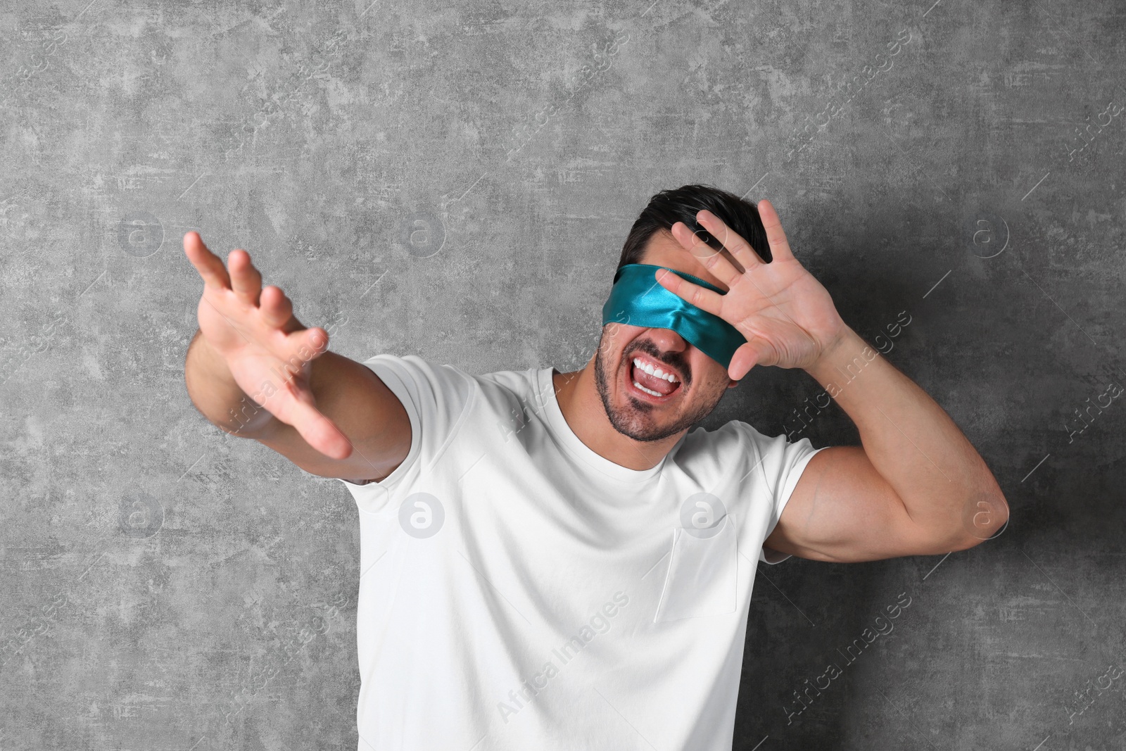 Photo of Young man wearing light blue blindfold on grey background