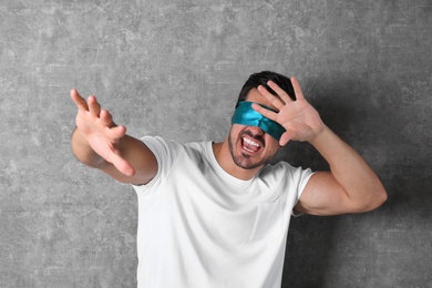 Young man wearing light blue blindfold on grey background