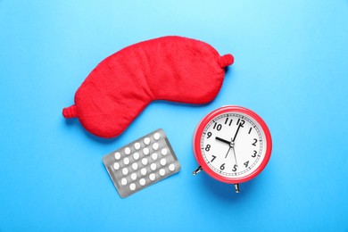 Photo of Soft sleep mask, blister of pills and alarm clock on light blue background, flat lay
