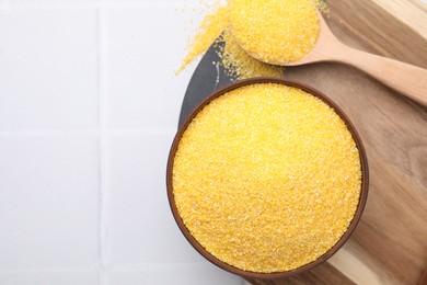Photo of Raw cornmeal in bowl and spoon on white tiled table, top view. Space for text