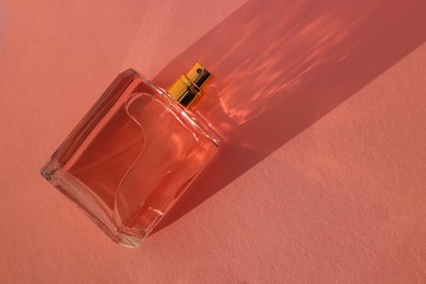 Photo of Luxury women's perfume. Sunlit glass bottle on pale pink background, top view. Space for text