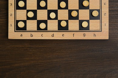 Photo of Checkerboard with game pieces on wooden table, top view. Space for text