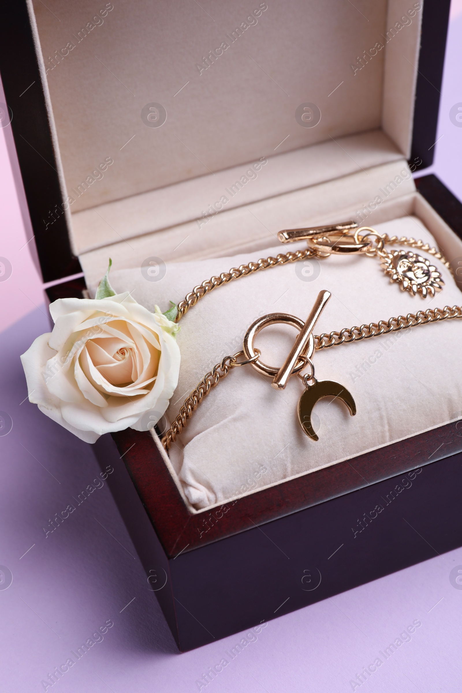 Photo of Beautiful jewelry and flower in box on violet background, closeup