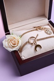 Photo of Beautiful jewelry and flower in box on violet background, closeup