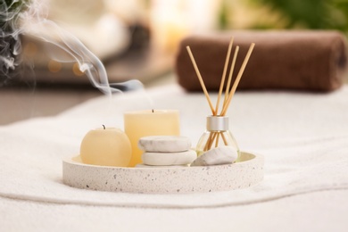 Photo of Composition with reed air freshener, candles and stones on massage table in spa salon