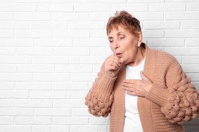 Photo of Elderly woman coughing near brick wall. Space for text