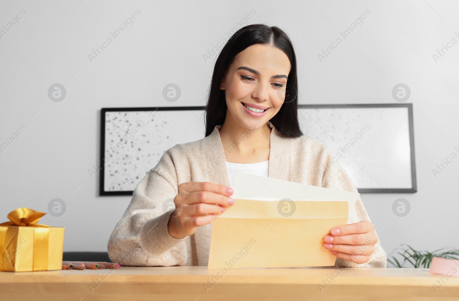 Photo of Happy woman reading greeting card at wooden table in room