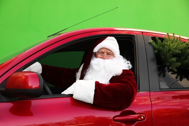 Photo of Authentic Santa Claus with fir tree driving car against green background