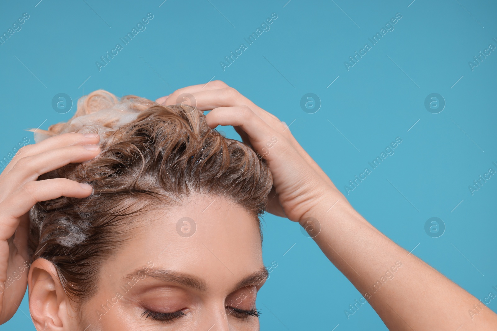 Photo of Woman washing hair on light blue background, closeup. Space for text