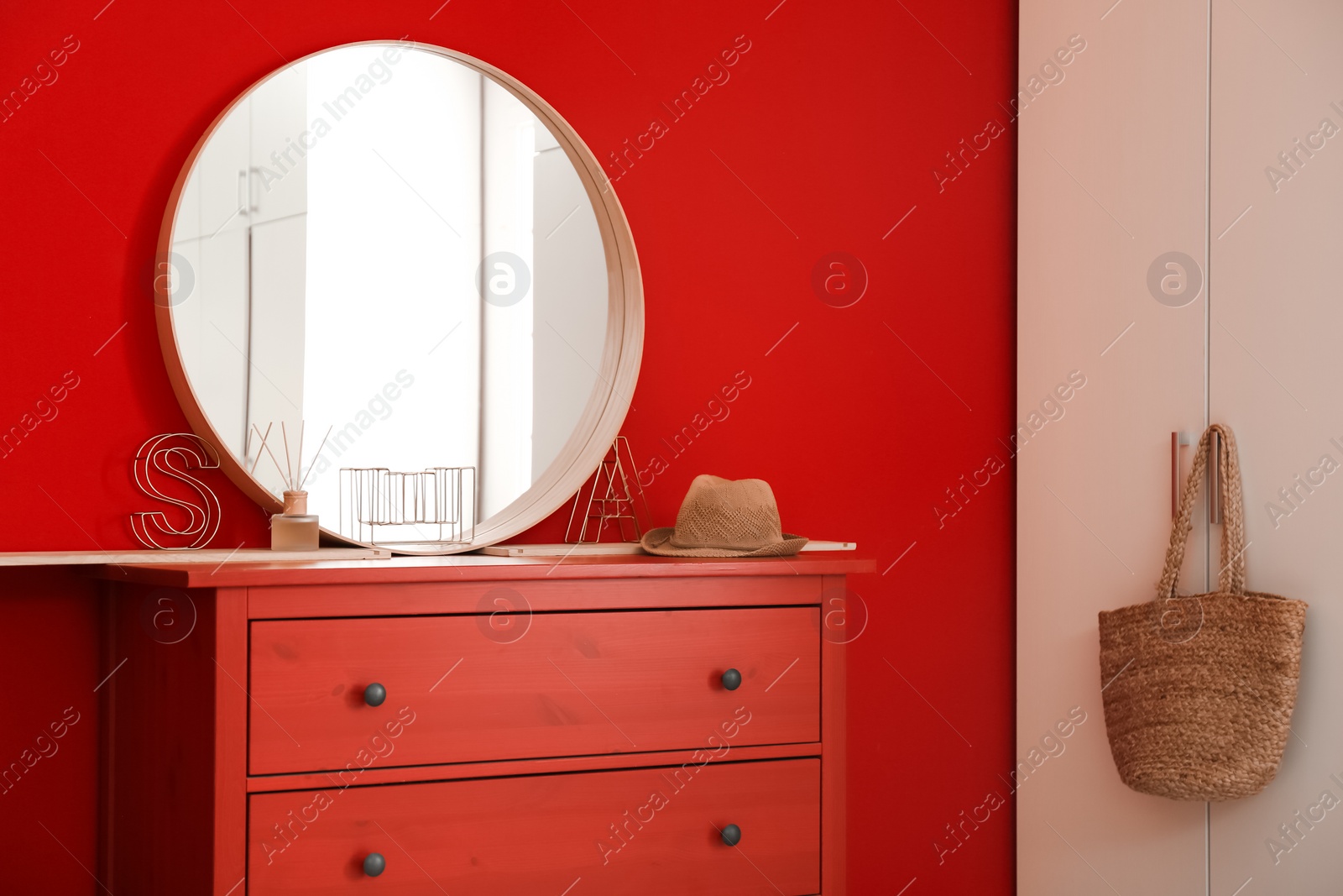 Photo of Round mirror and chest of drawers near red wall in room. Modern interior design