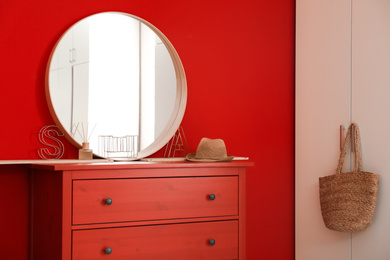 Photo of Round mirror and chest of drawers near red wall in room. Modern interior design