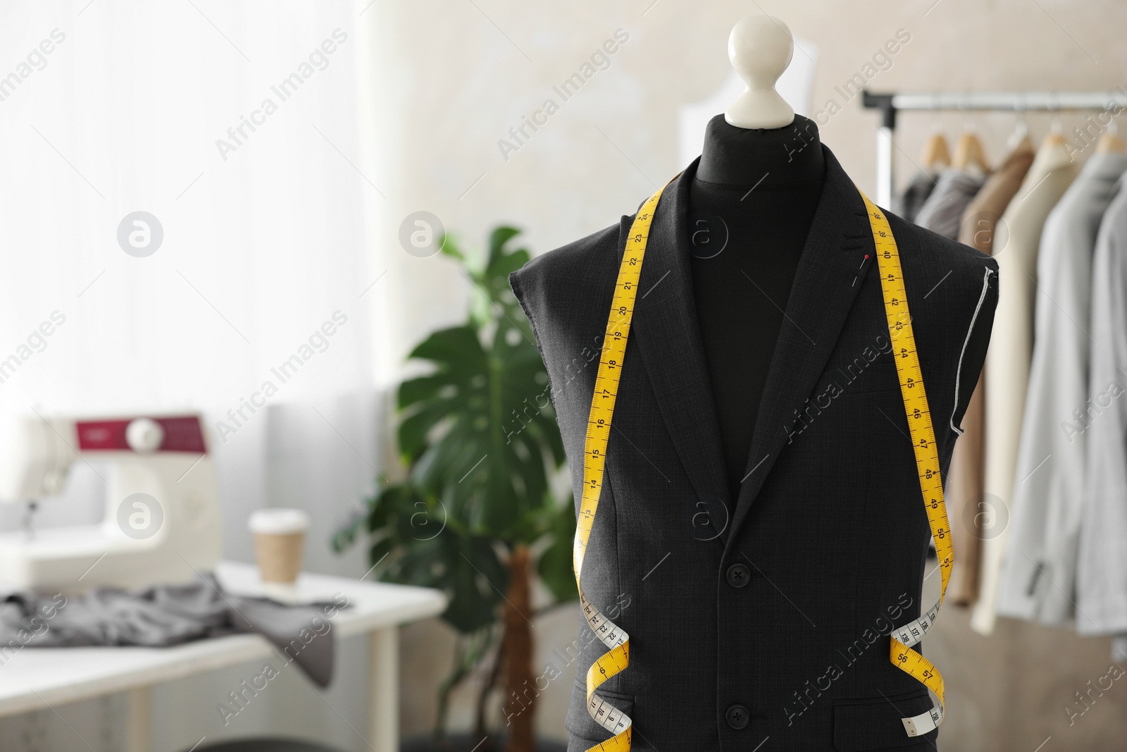 Photo of Mannequin with unfinished suit jacket and measuring tape in tailor shop, space for text