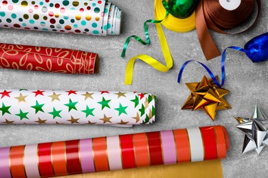 Photo of Different colorful wrapping paper rolls, gift bows and ribbons on grey table, flat lay