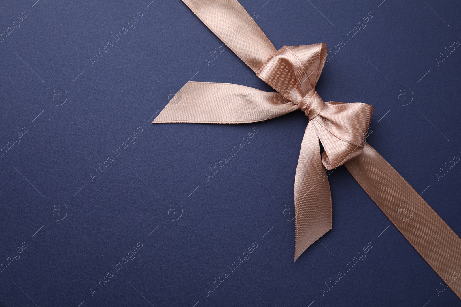 Photo of Beige satin ribbon with bow on blue background, top view. Space for text