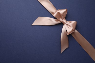 Beige satin ribbon with bow on blue background, top view. Space for text