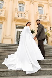 Photo of Young bride and groom on stairs outdoors, low angle view. Wedding couple