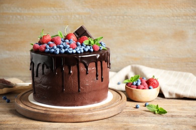 Photo of Freshly made delicious chocolate cake decorated with berries on wooden table