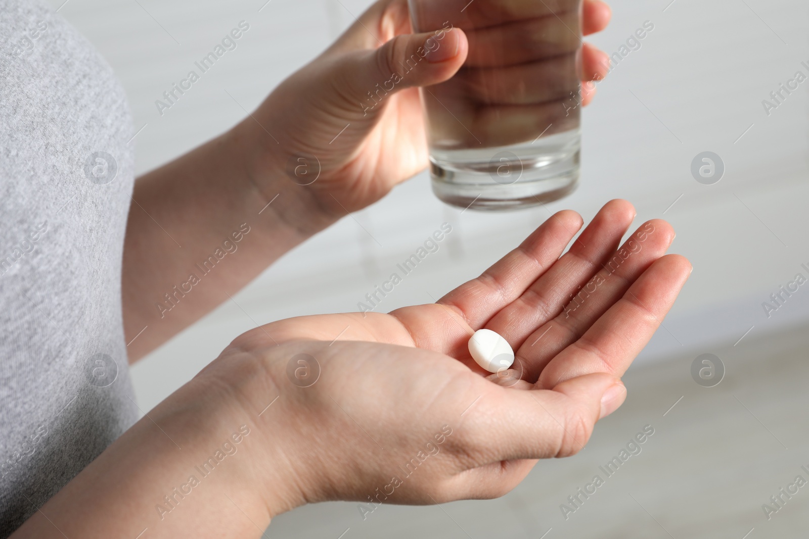 Photo of Woman with glass of water and pill on blurred background, closeup