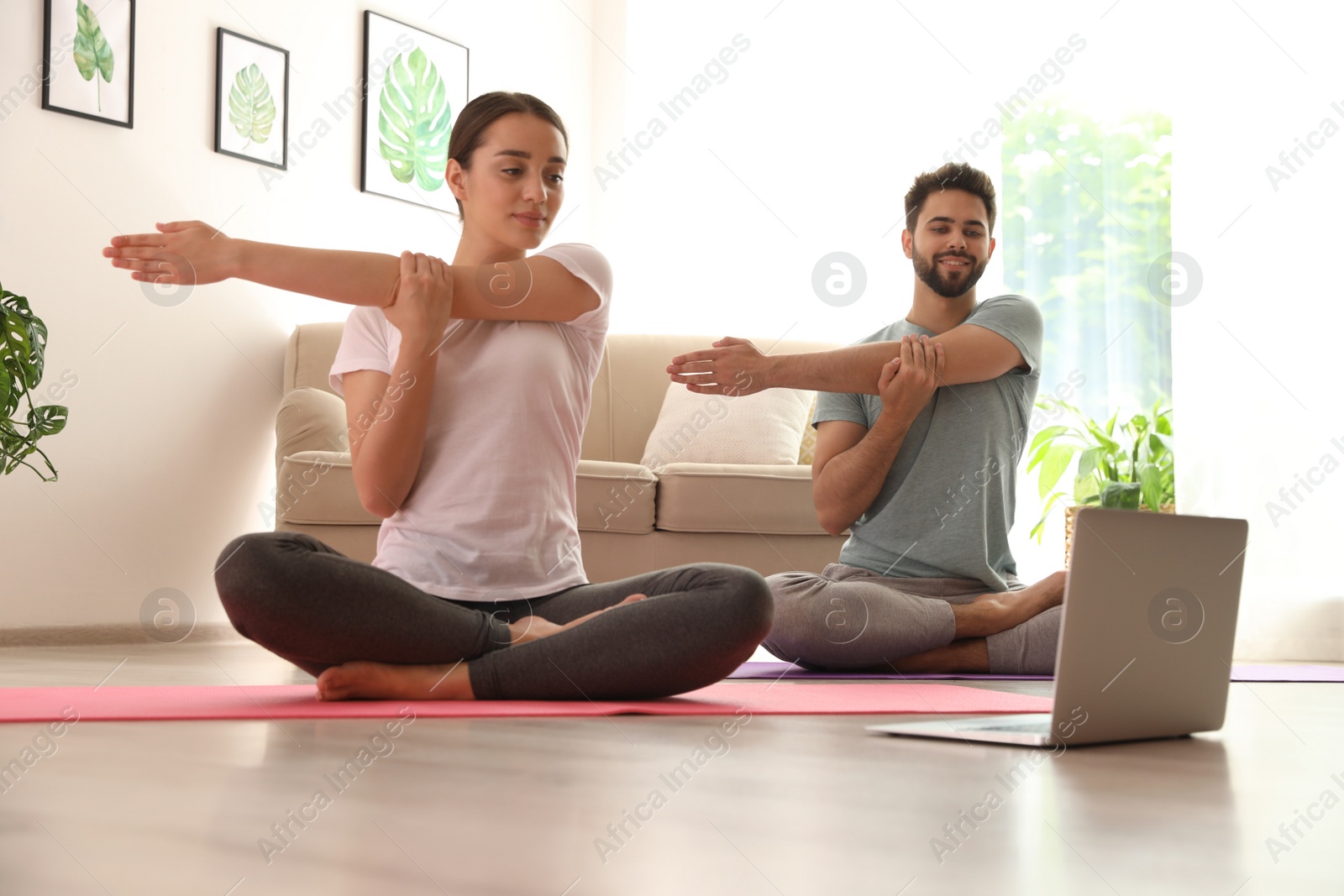 Photo of Couple practicing yoga while watching online class at home during coronavirus pandemic. Social distancing