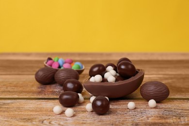 Photo of Delicious chocolate eggs and candies on wooden table against yellow background