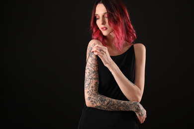 Beautiful woman with tattoos on arms against black background. Space for text