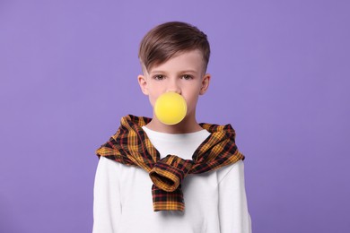 Boy blowing bubble gum on purple background