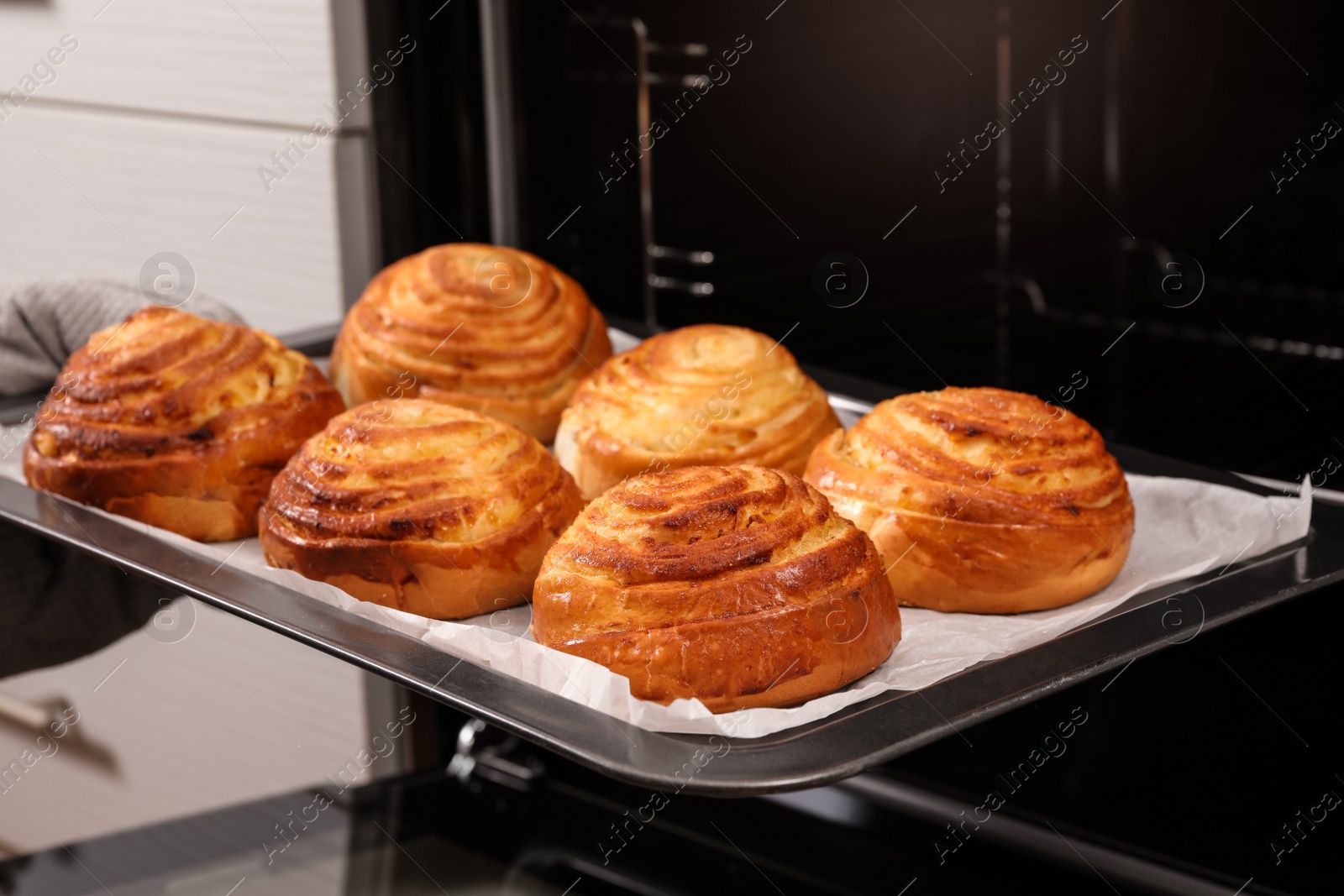 Photo of Woman taking freshly baked buns out of oven, closeup