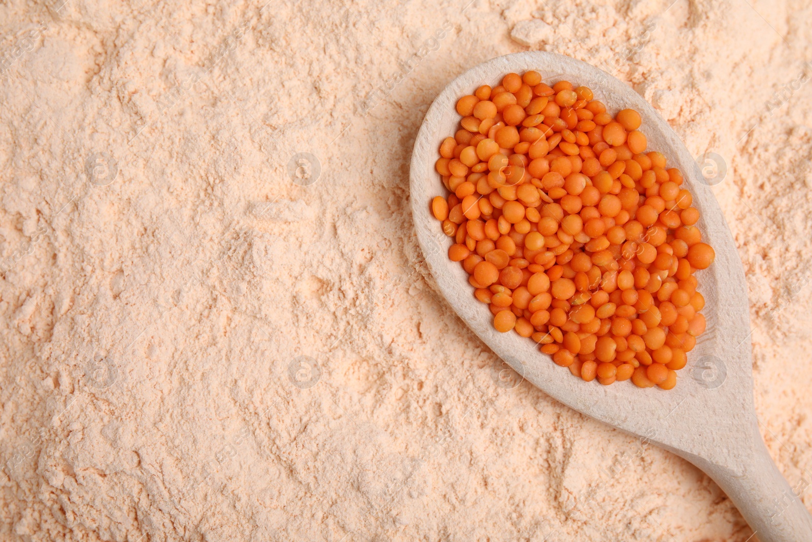 Photo of Spoon with lentil grains on flour, top view. Space for text