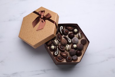 Open box of delicious chocolate candies on white marble table, top view