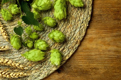 Photo of Wicker mat with fresh green hops and wheat ears on wooden table, top view