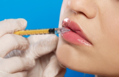 Photo of Young woman getting lips injection on color background, closeup. Cosmetic surgery