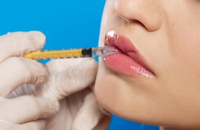 Young woman getting lips injection on color background, closeup. Cosmetic surgery