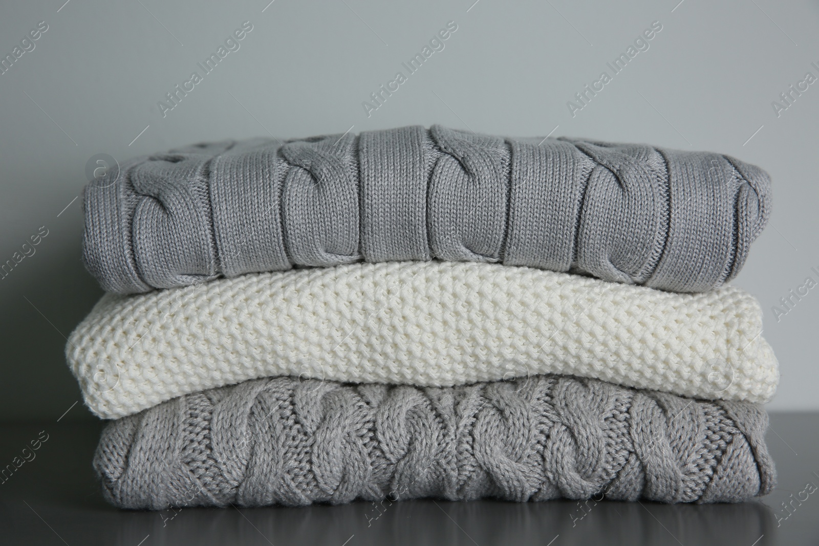 Photo of Stack of folded knitted sweaters on grey table, closeup