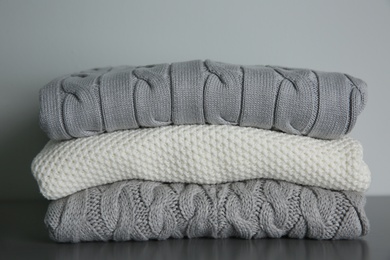 Stack of folded knitted sweaters on grey table, closeup