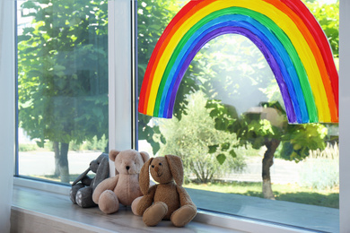 Photo of Painting of rainbow on window and toys indoors. Stay at home concept