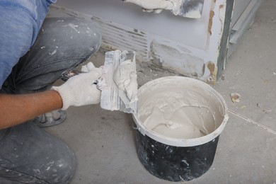 Photo of Worker plastering wall with putty knife indoors, closeup