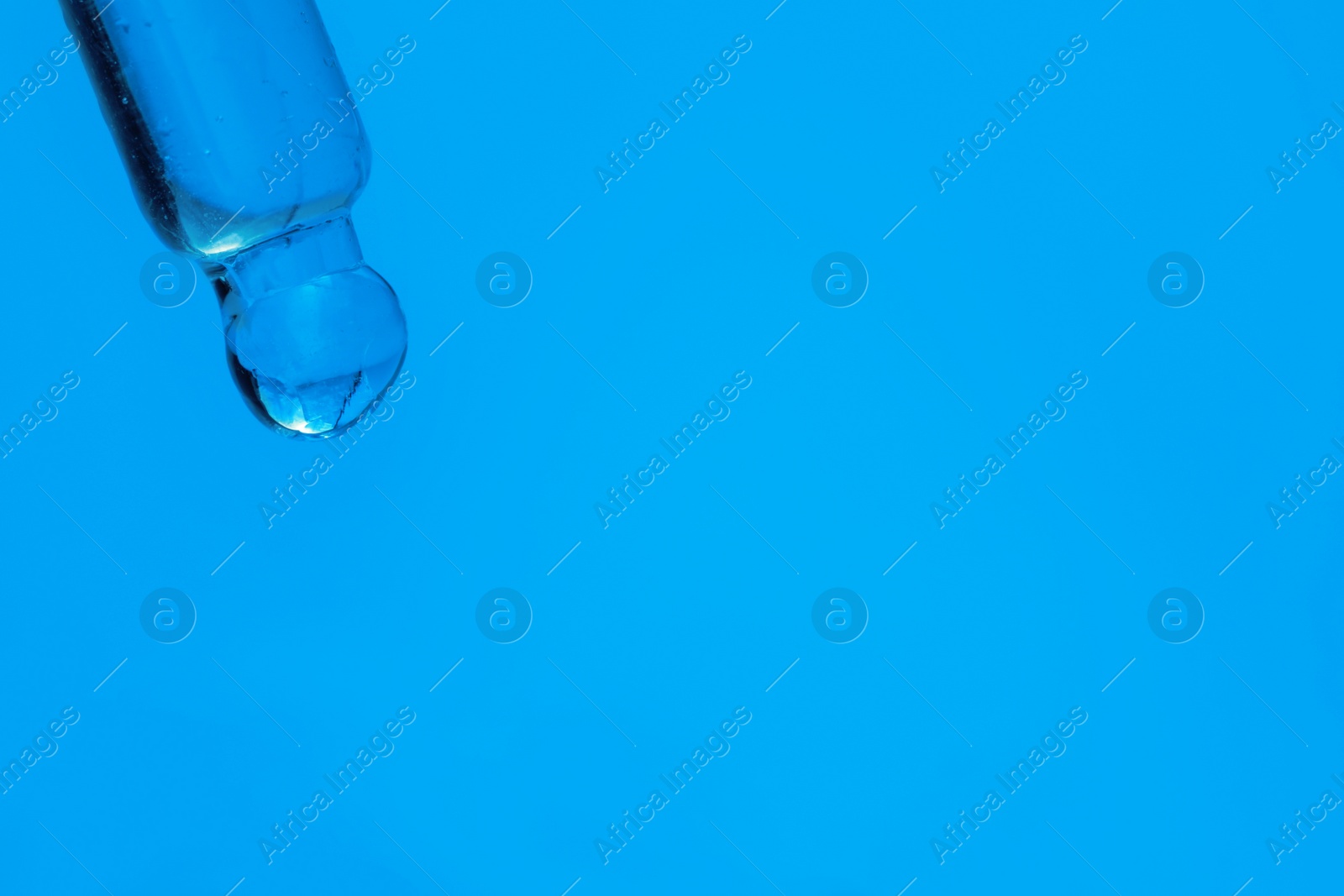 Photo of Dripping face serum from pipette on blue background, closeup. Space for text