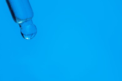 Photo of Dripping face serum from pipette on blue background, closeup. Space for text