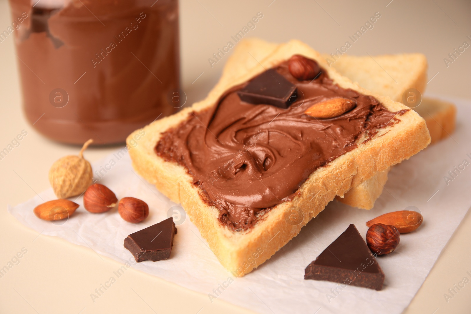 Photo of Tasty toast with chocolate paste and nuts near jar of cream on light table, closeup