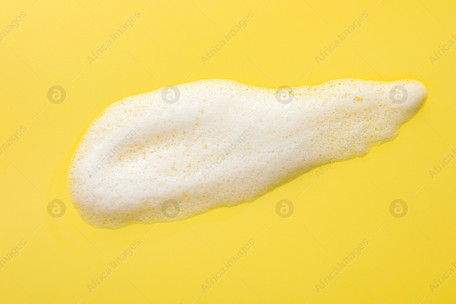 Photo of Drop of fluffy soap foam on yellow background, top view