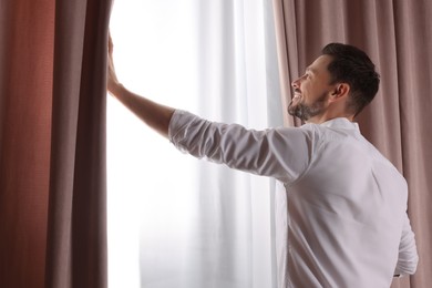 Happy man opening window curtains at home