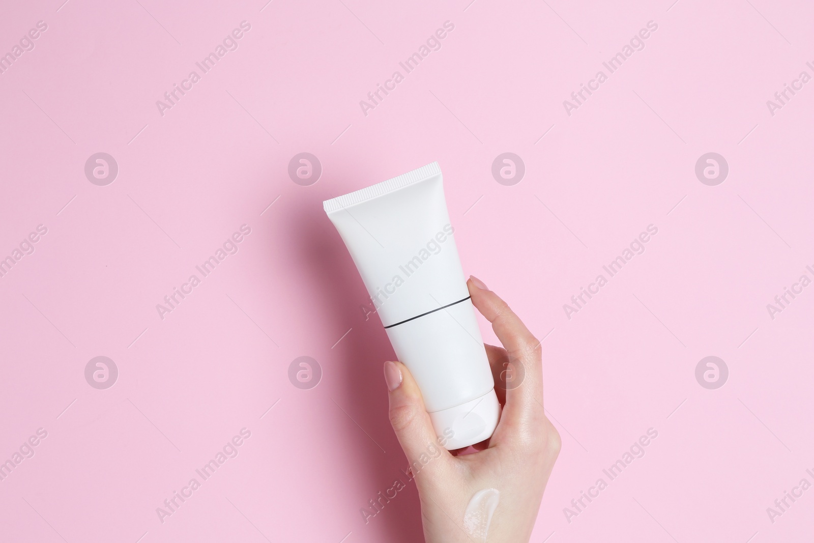 Photo of Woman holding tube of cream on pink background, closeup