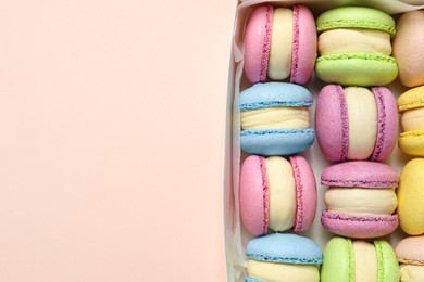 Photo of Many delicious colorful macarons in box on pink background, top view. Space for text