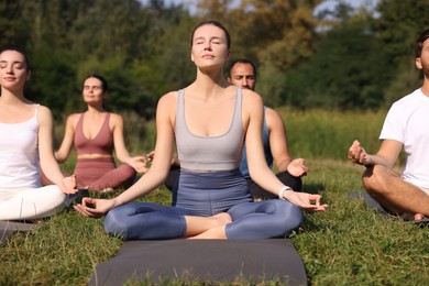 Group of people practicing yoga on mats outdoors. Lotus pose