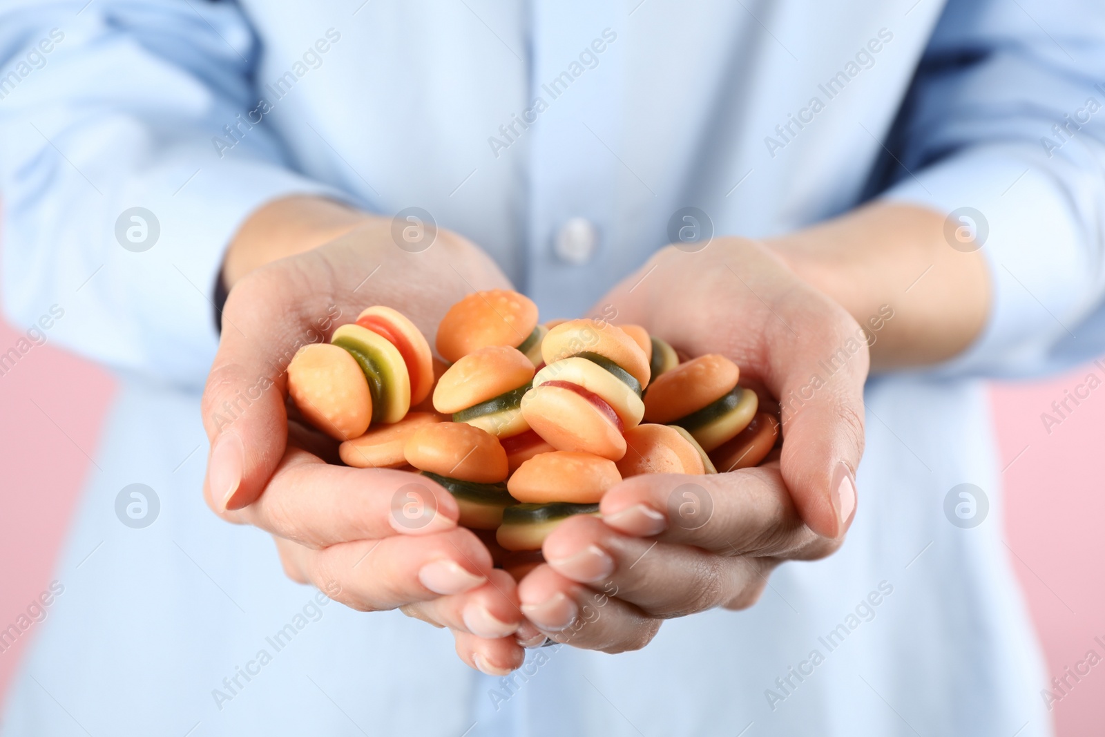 Photo of Woman holding handful of delicious gummy burger shaped candies on pink background, closeup